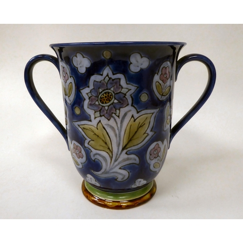 73 - An early 20thC Doulton stoneware twin handled loving cup, decorated with stylised floral designs, on... 