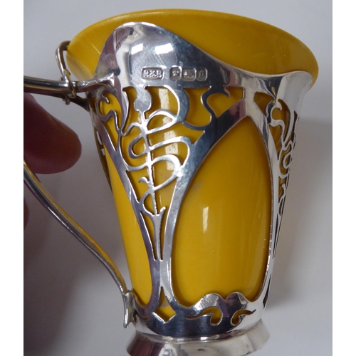 93 - An Edwardian yellow china coffee can, in a decoratively pierced silver frame with a handle, attendan... 