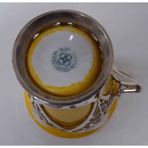 93 - An Edwardian yellow china coffee can, in a decoratively pierced silver frame with a handle, attendan... 