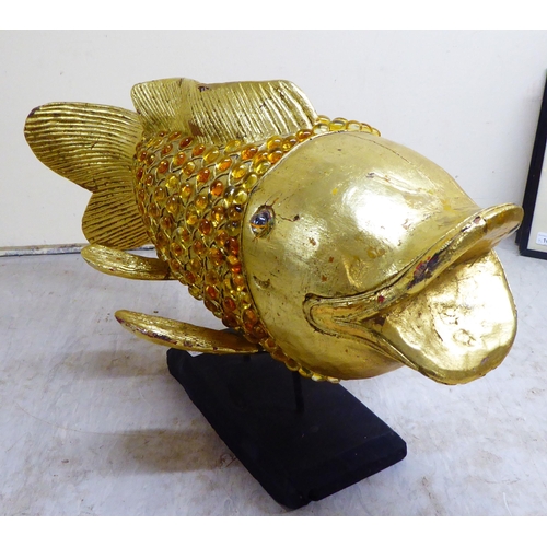 151 - A modern antique finished, gilt painted, carved wooden and amber coloured model carp, on stilts and ... 