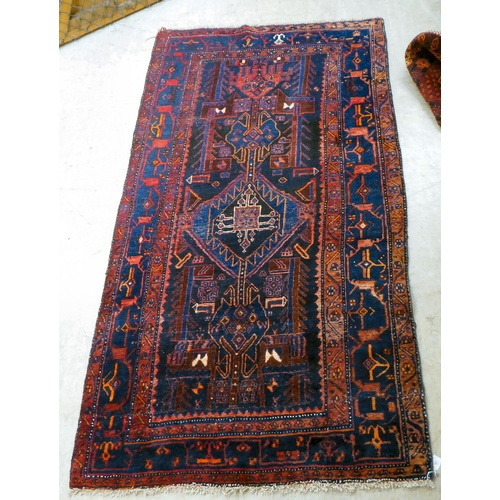 63 - A Persian rug, decorated with central stylised designs, bordered by abstract shapes, on a dark blue ... 