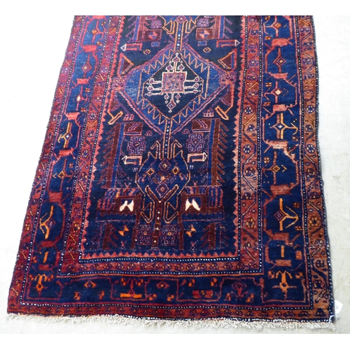 63 - A Persian rug, decorated with central stylised designs, bordered by abstract shapes, on a dark blue ... 