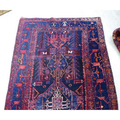 63 - A Persian rug, decorated with central stylised designs, bordered by abstract shapes, on a dark blue ... 