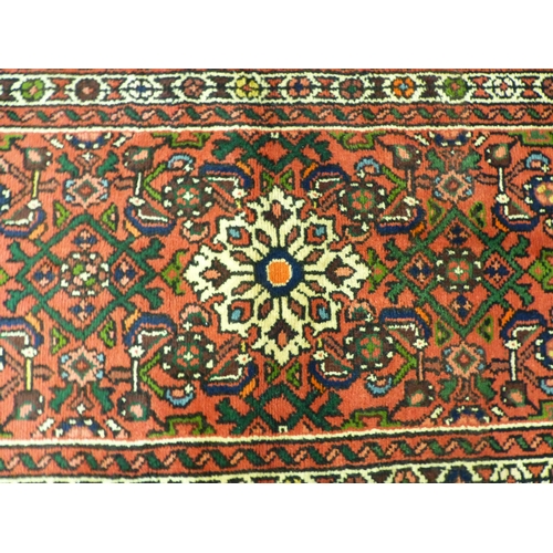 76 - A Hamadan design runner, decorated with a central medallion and floral motifs, on a red ground ... 