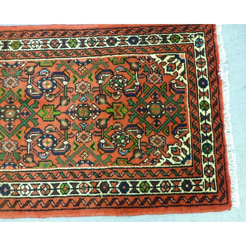 76 - A Hamadan design runner, decorated with a central medallion and floral motifs, on a red ground ... 