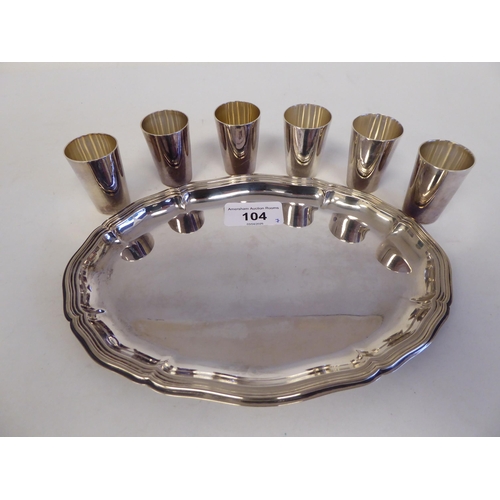 104 - A silver coloured metal liqueur set, comprising six tumbler cups, on an oval, wavy edged tray&nbsp; ... 