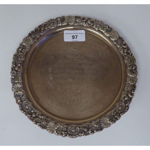 97 - An Edwardian silver waiter with a raised shell and scroll cast border, on conforming feet  bears a p... 