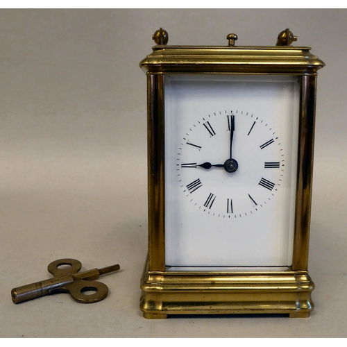 32 - A lacquered brass travel clock with bevelled glass panels; the gong strike movement faced by an enam... 
