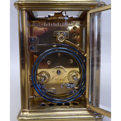 32 - A lacquered brass travel clock with bevelled glass panels; the gong strike movement faced by an enam... 