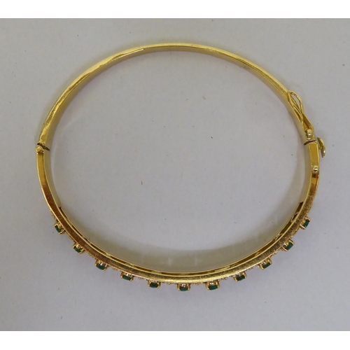 48 - A yellow metal (probably 18ct gold) hinged bangle, set with alternating emeralds and diamonds  (appr... 