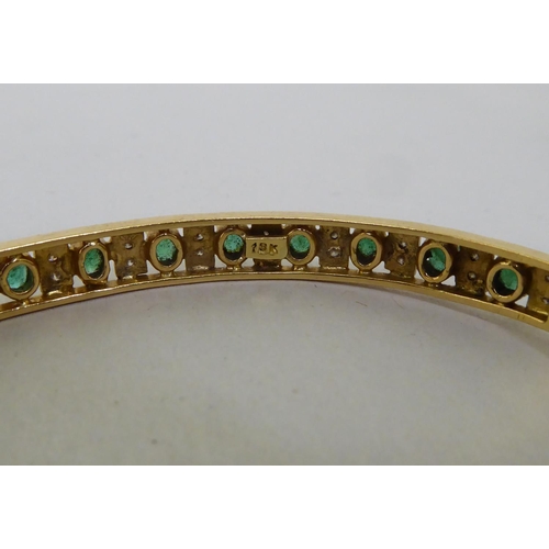 48 - A yellow metal (probably 18ct gold) hinged bangle, set with alternating emeralds and diamonds  (appr... 