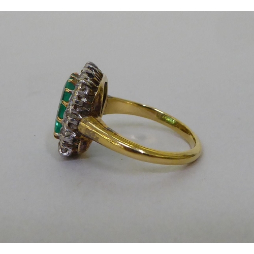 51 - A yellow metal (probably 18ct gold) cluster ring, set with a central emerald, surrounded by diamonds... 