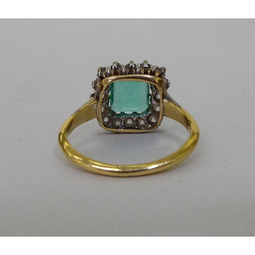 51 - A yellow metal (probably 18ct gold) cluster ring, set with a central emerald, surrounded by diamonds... 