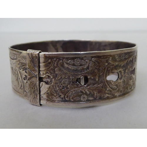 61 - A silver buckle bangle, decorated with floral motifs&nbsp; marks rubbed