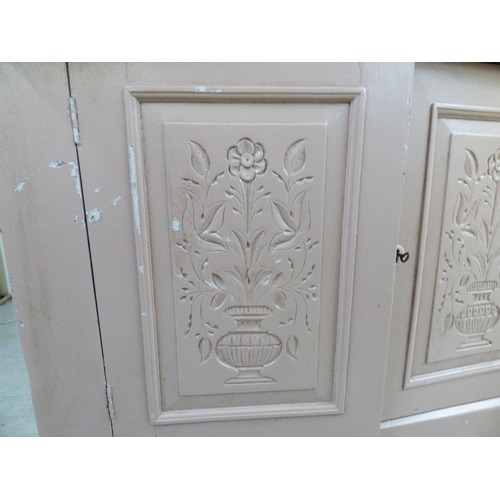 24 - An early 20thC pink painted pine chiffonier with a frieze drawer, over a pair of floral carved panel... 