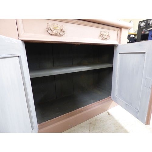 24 - An early 20thC pink painted pine chiffonier with a frieze drawer, over a pair of floral carved panel... 