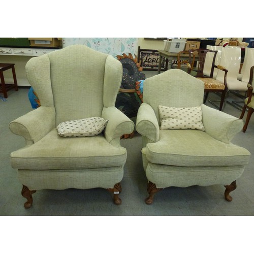 60 - Two similar modern wingback arm chairs, upholstered in beige fabric, raised on cabriole legs