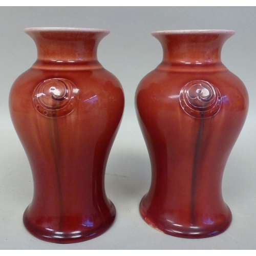 39 - A pair of Moorcroft pottery Liberty vases, each decorated with Art Nouveau floral motifs, on a red g... 