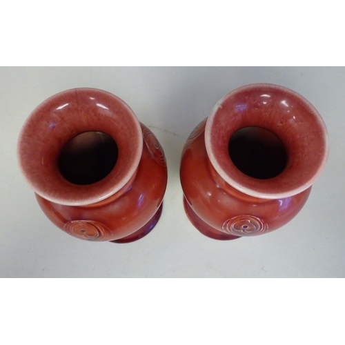 39 - A pair of Moorcroft pottery Liberty vases, each decorated with Art Nouveau floral motifs, on a red g... 