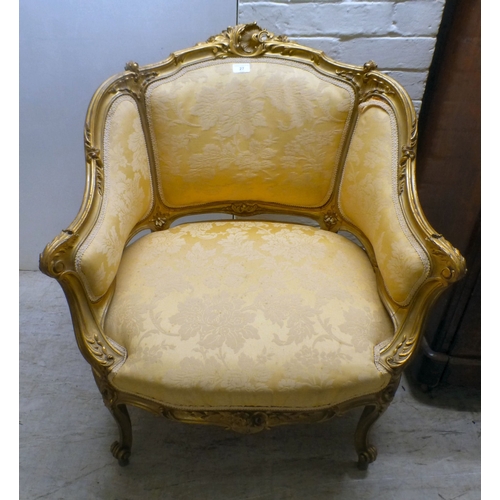 27 - A 20thC reproduction of an 18thC Continental gilt sprayed showwood salon chair, upholstered in flora... 