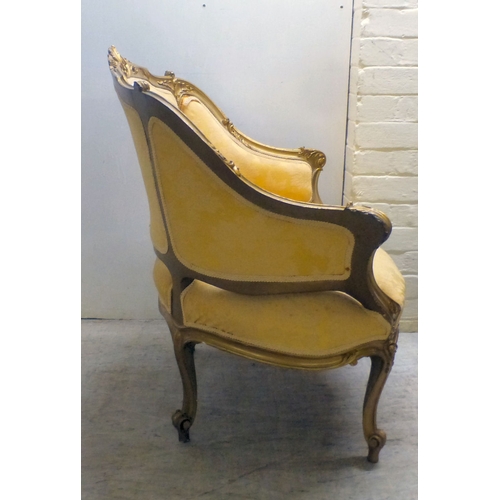 27 - A 20thC reproduction of an 18thC Continental gilt sprayed showwood salon chair, upholstered in flora... 