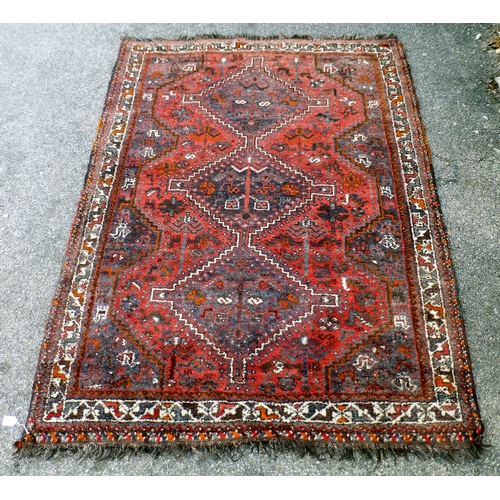120 - A Persian rug, decorated with three central diamond shaped motifs, bordered by stylised designs, on ... 