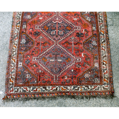 120 - A Persian rug, decorated with three central diamond shaped motifs, bordered by stylised designs, on ... 