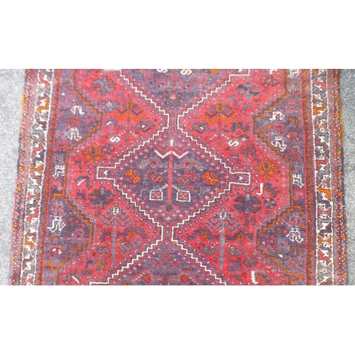 120 - A Persian rug, decorated with three central diamond shaped motifs, bordered by stylised designs, on ... 