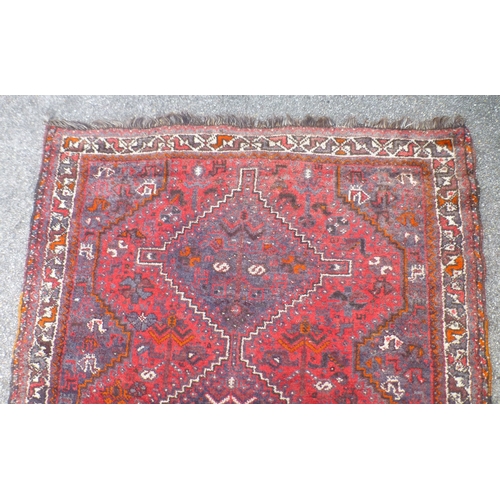 120 - A Persian rug, decorated with three central diamond shaped motifs, bordered by stylised designs, on ... 