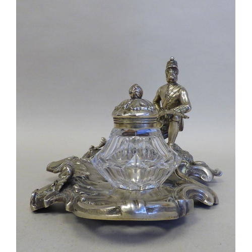 19 - An early 20thC cast white metal inkstand, surmounted by a white metal on copper military figure, kne... 
