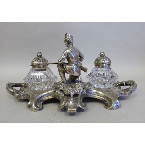 19 - An early 20thC cast white metal inkstand, surmounted by a white metal on copper military figure, kne... 