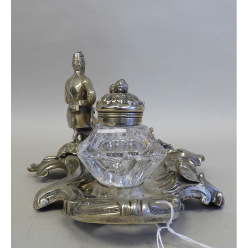 19 - An early 20thC cast white metal inkstand, surmounted by a white metal on copper military figure, kne... 