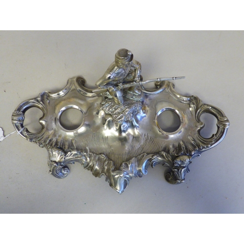19 - An early 20thC cast white metal inkstand, surmounted by a white metal on copper military figure, kne... 