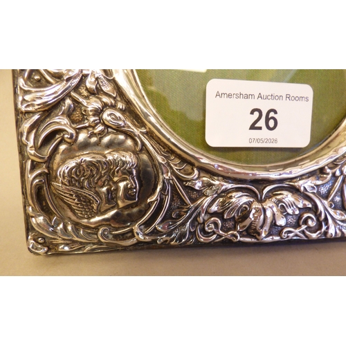 26 - A George V Victorian style, silver pressed photograph frame with cherubic/angelic and foliage orname... 