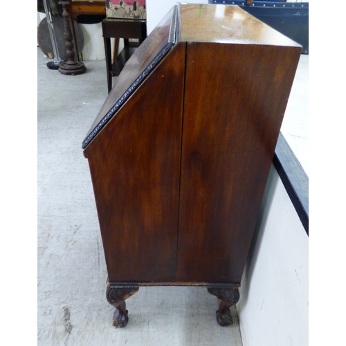 44 - An early 20thC mahogany bureau with a fall flap, over three graduated drawers, raised on carved, stu... 