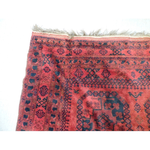 45 - An Afghan rug, decorated with hexagonal guls, stylised designs and a border, on a red ground  64
