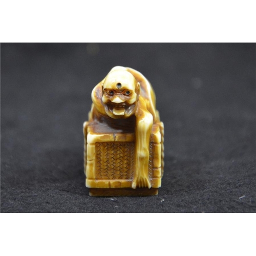 125 - λ A Japanese carved ivory netsuke, Meiji, 19th century, modelled as an emaciated figure on a box, st... 