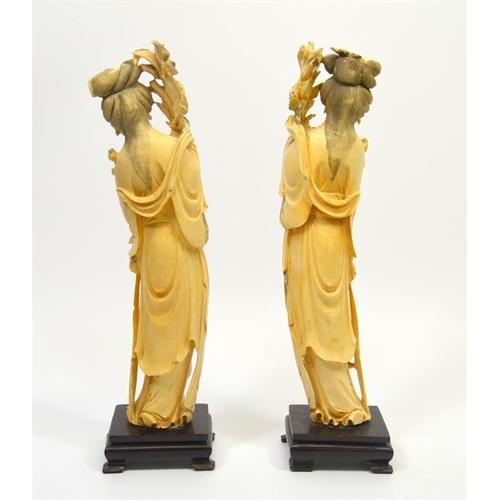 129 - A pair of Chinese carved ivory figures, 19th century, modelled as women holding lotus flowers, on st... 