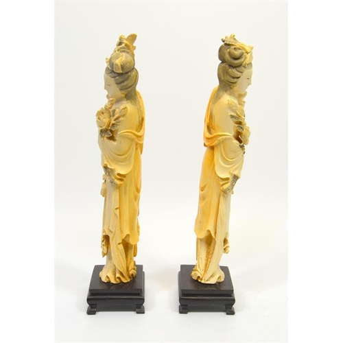 129 - A pair of Chinese carved ivory figures, 19th century, modelled as women holding lotus flowers, on st... 