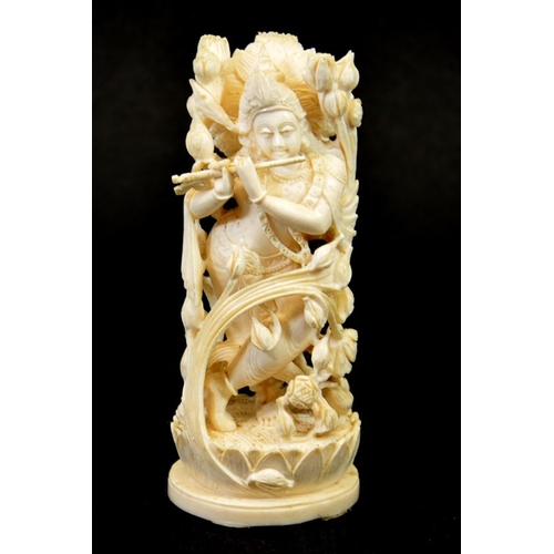 32 - λ A 19th century Indian carved ivory figure of a deity playing the pipe, within a floral cage, stand... 