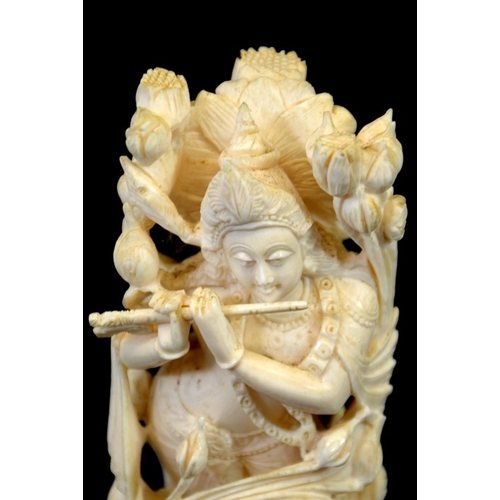 32 - λ A 19th century Indian carved ivory figure of a deity playing the pipe, within a floral cage, stand... 