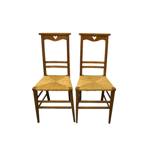 150 - A pair of Arts and Crafts oak chairs, cut-out heart motif to top rail on backs and rush seats, 91cm ... 