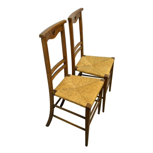 150 - A pair of Arts and Crafts oak chairs, cut-out heart motif to top rail on backs and rush seats, 91cm ... 