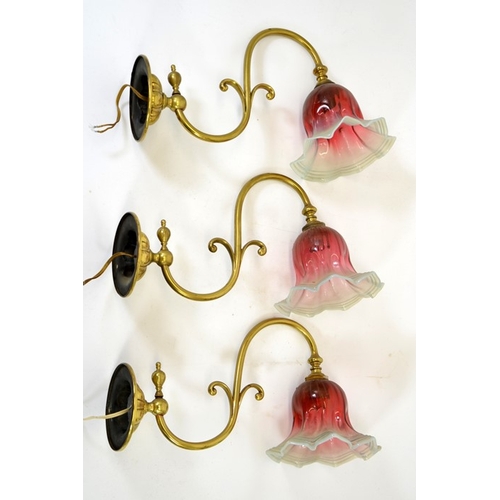 236 - Three Arts and Crafts wall mounted brass lights, with opalescent and cranberry glass shades, the arm... 