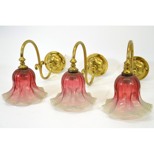 236 - Three Arts and Crafts wall mounted brass lights, with opalescent and cranberry glass shades, the arm... 