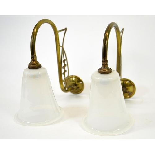 244 - A pair of Art Nouveau brass wall lights, with opaque glass shades, the curved arms with open stylise... 