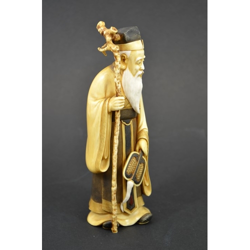 49 - λ A 19th century Japanese carved ivory okimino of an elder, Meiji, modelled holding a staff and fan,... 