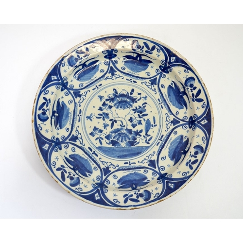 1317 - A Delft blue and white charger, circa 1740, painted with a central floral design within foliate oval... 