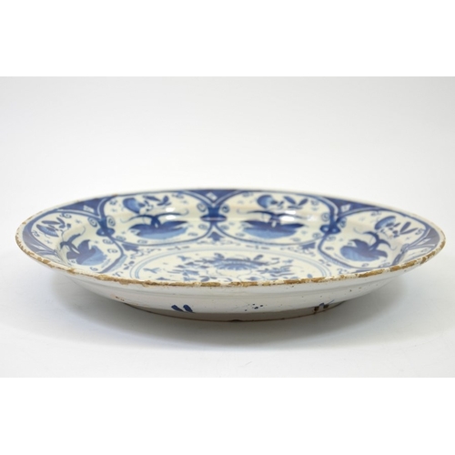 1317 - A Delft blue and white charger, circa 1740, painted with a central floral design within foliate oval... 