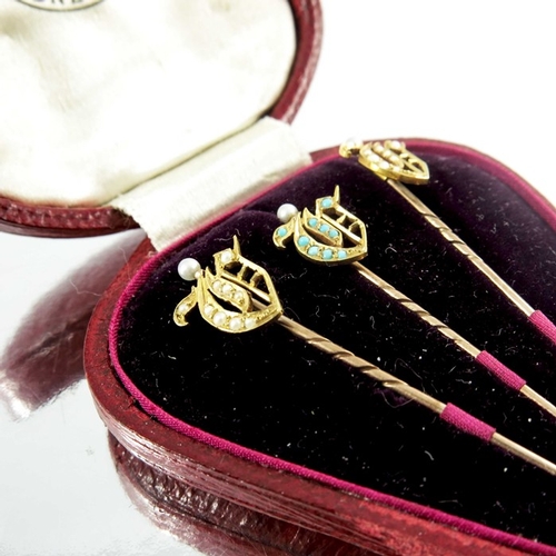 117 - A cased set of three yellow gold gem set shield stickpins, two mounted with pearls, the third mounte... 